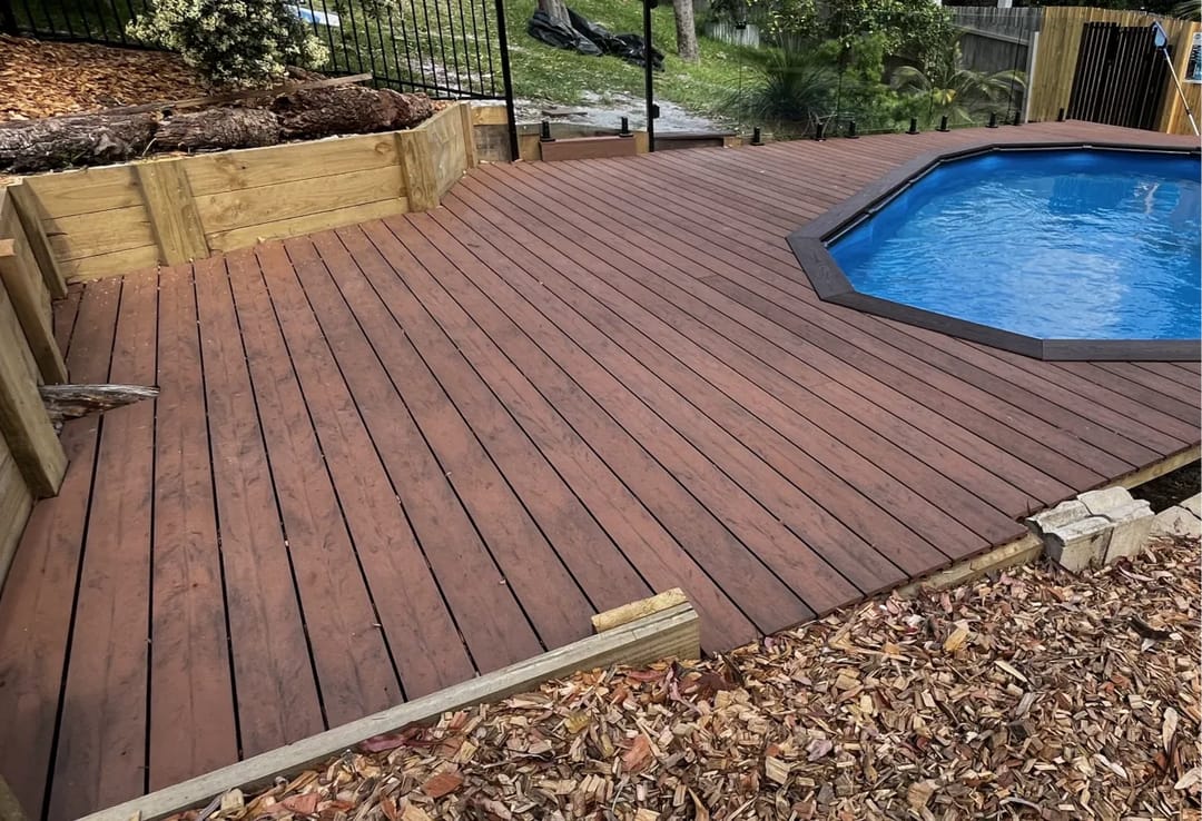 Backyard deck in CleverDeck Eco-Pro Black Bean around a round above-ground pool, edged with timber sleepers and mulch