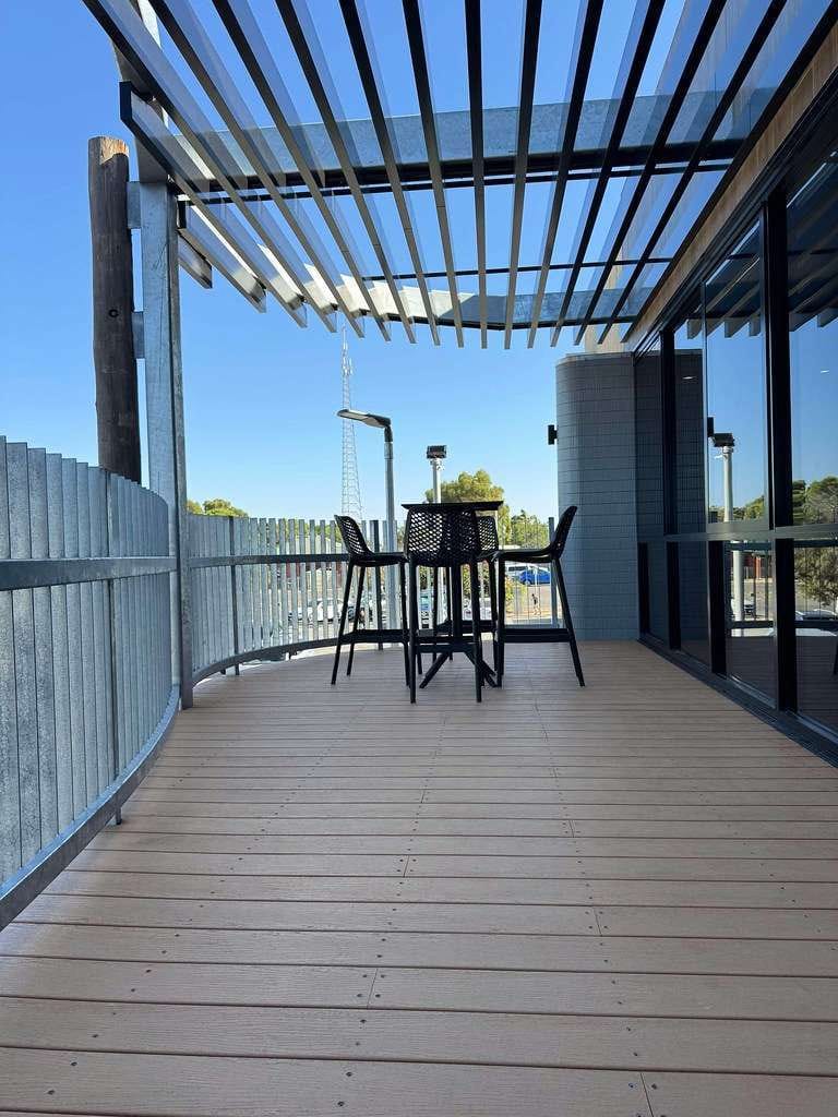 Balcony deck in ModWood Xtreme Guard Koko Brown under a louvred roof, with a bar table and stools
