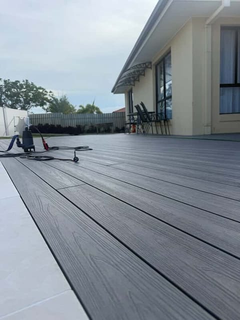 Dark grey composite deck meeting pale pool tiles beside a rendered home, with grain running along the boards