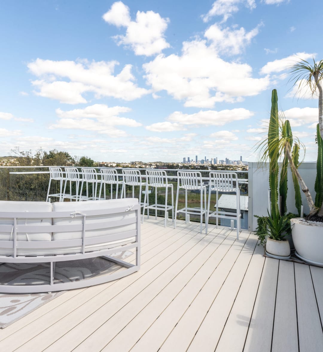 Pale WoodEvo HOME composite deck on a rooftop terrace with white outdoor seating, potted cacti and city skyline views