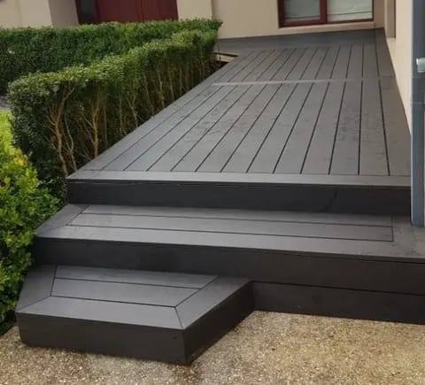 Low-height front deck and two wide steps in dark CleverDeck Xtreme Graphite 138 mm boards beside a clipped hedge