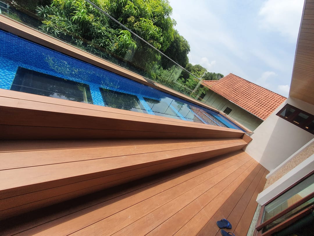Biowood deck and stepped edge in honey-brown boards beside a raised blue-tiled pool, under a tiled roof