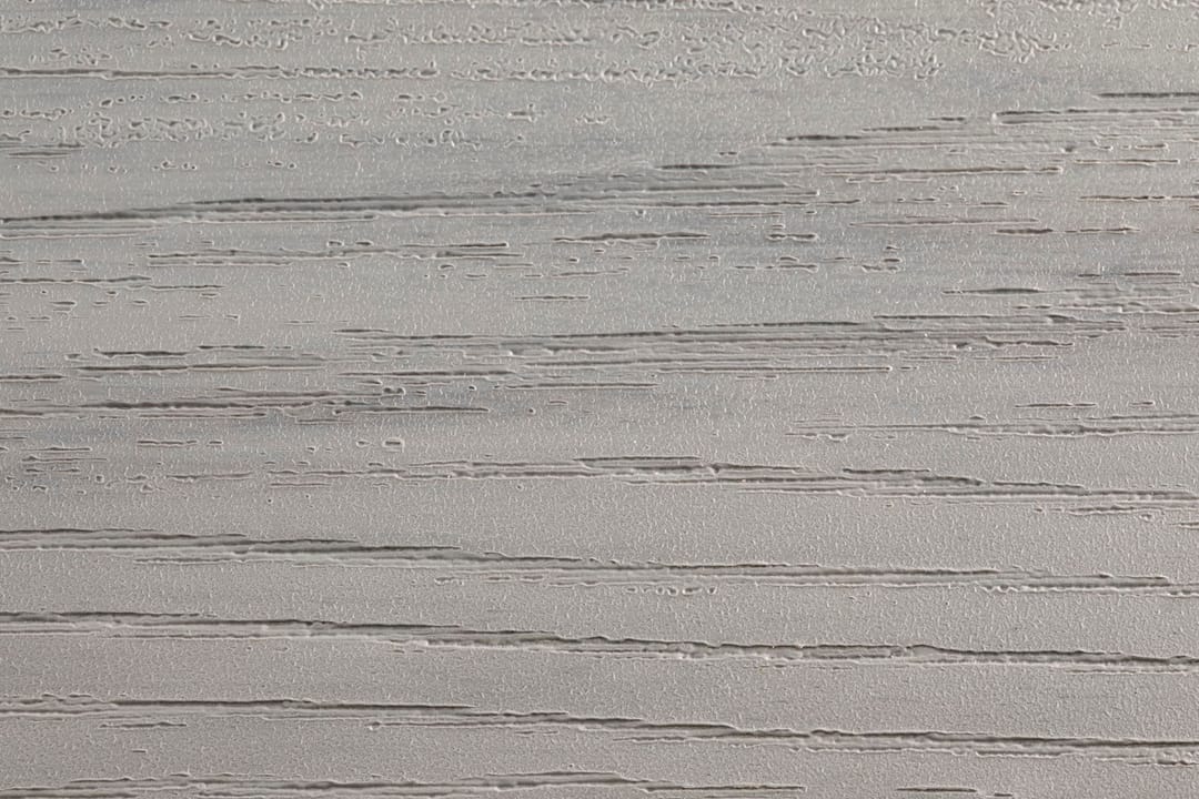 Close-up of an Evertex Supreme Max Coral Grey board surface showing its embossed wood-grain texture in soft grey
