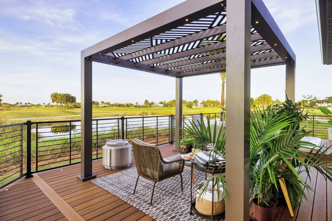Havana Gold deck under a slatted metal pergola with wicker chairs, a rug and potted palms, overlooking wetland