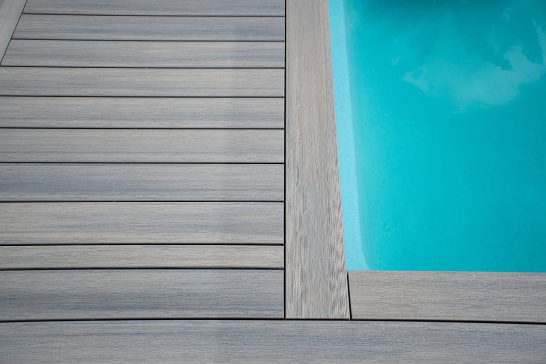 Grey WoodEvo composite decking boards laid around a blue swimming pool, with a picture-frame border at the pool edge