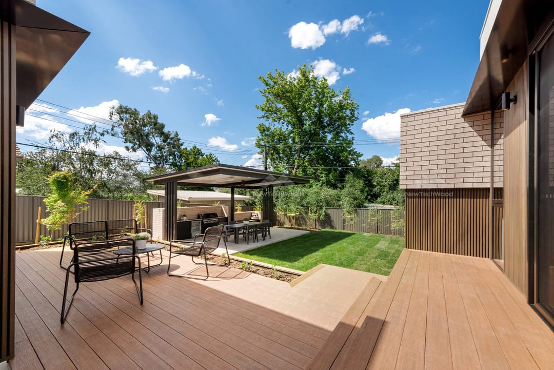 NewTechWood Terrace Teak deck with outdoor furniture, a pergola and lawn, beside Aged Wood castellation cladding