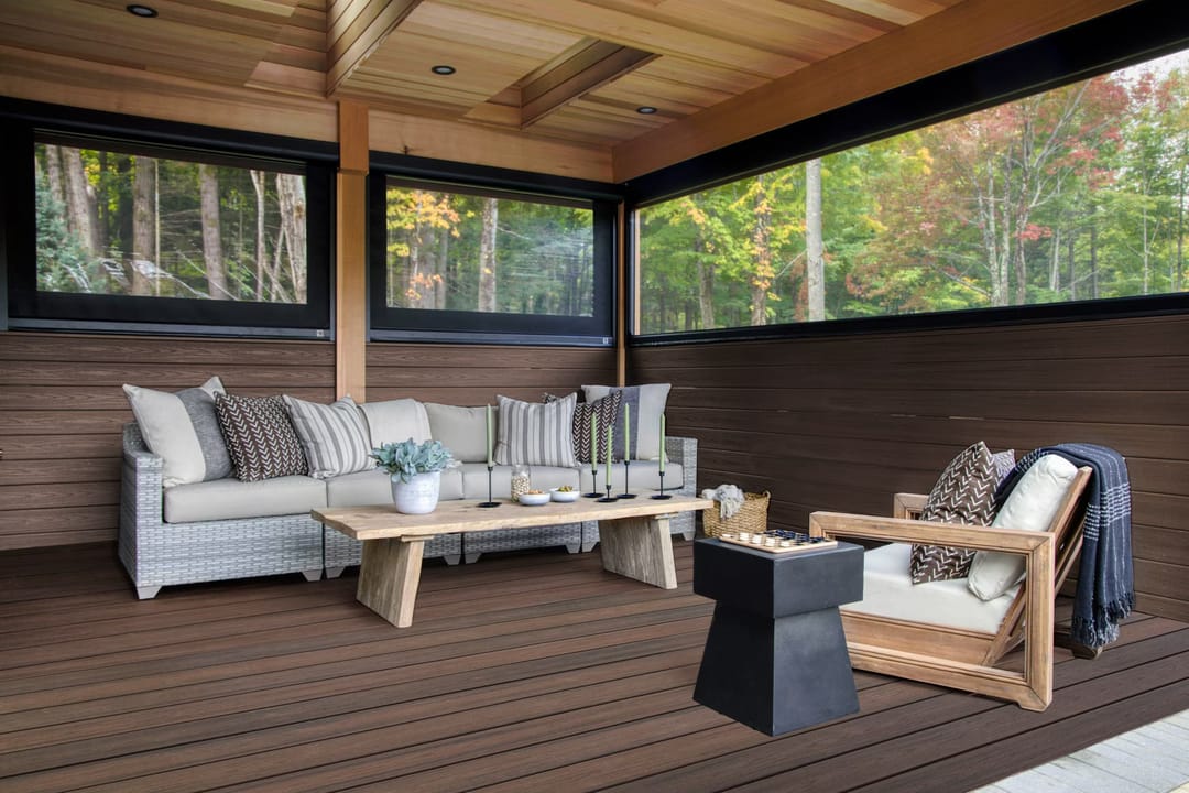 Dark brown Spiced Rum decking in a screened porch with a sectional sofa, armchair and coffee table, woods outside