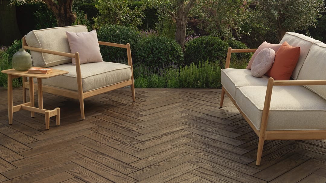 Antique Oak decking laid in herringbone under a timber sofa and armchair with cushions, in a leafy garden