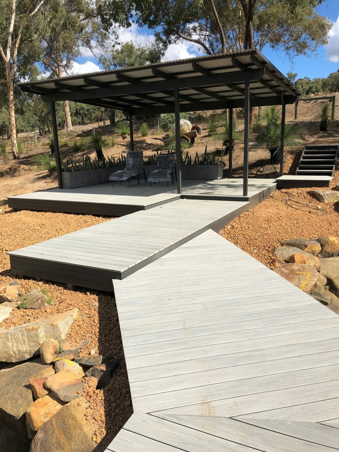 Light grey composite boardwalk zig-zagging up a rocky slope to a pergola-covered deck at Gidgegannup, WA