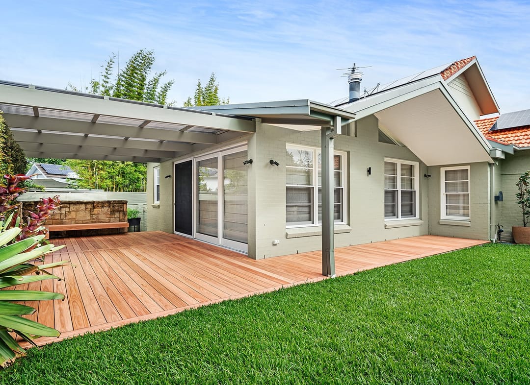 Backyard deck in Eva-Last Pioneer under a covered pergola beside a grey weatherboard house and a green lawn