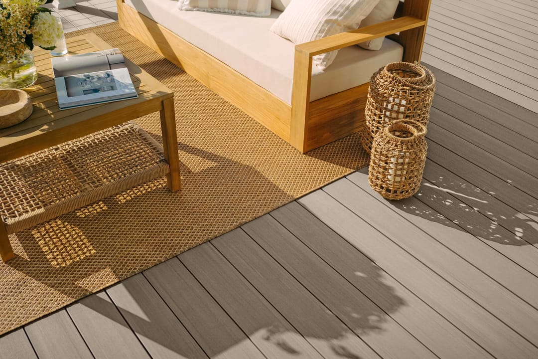 Close view of grey Coastline decking under a jute rug, a timber-framed sofa, coffee table and woven lanterns