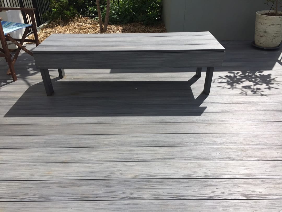 Grey Sun Decking Elite Harbour Grey deck with a low dark outdoor table, a timber chair and potted plants