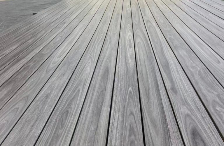 Low-angle close-up of laid Origin Greyed Spotted Gum composite deck boards in weathered silver-grey tones