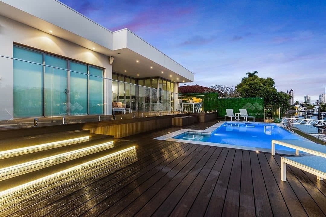 Dark NewTechWood Terrace Ipe deck with LED-lit steps beside a pool and modern home at dusk