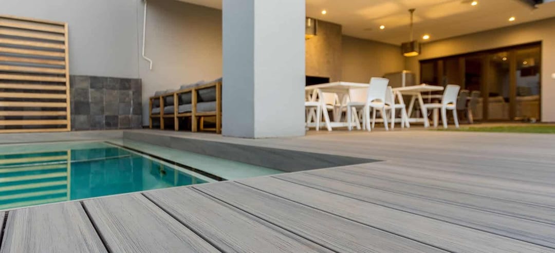 Vision decking around a small plunge pool outside an open-plan living and dining room with warm lighting