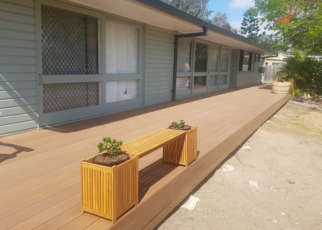 Long Sun Decking Elite Teak deck running along a weatherboard house, with a timber planter bench in the sun