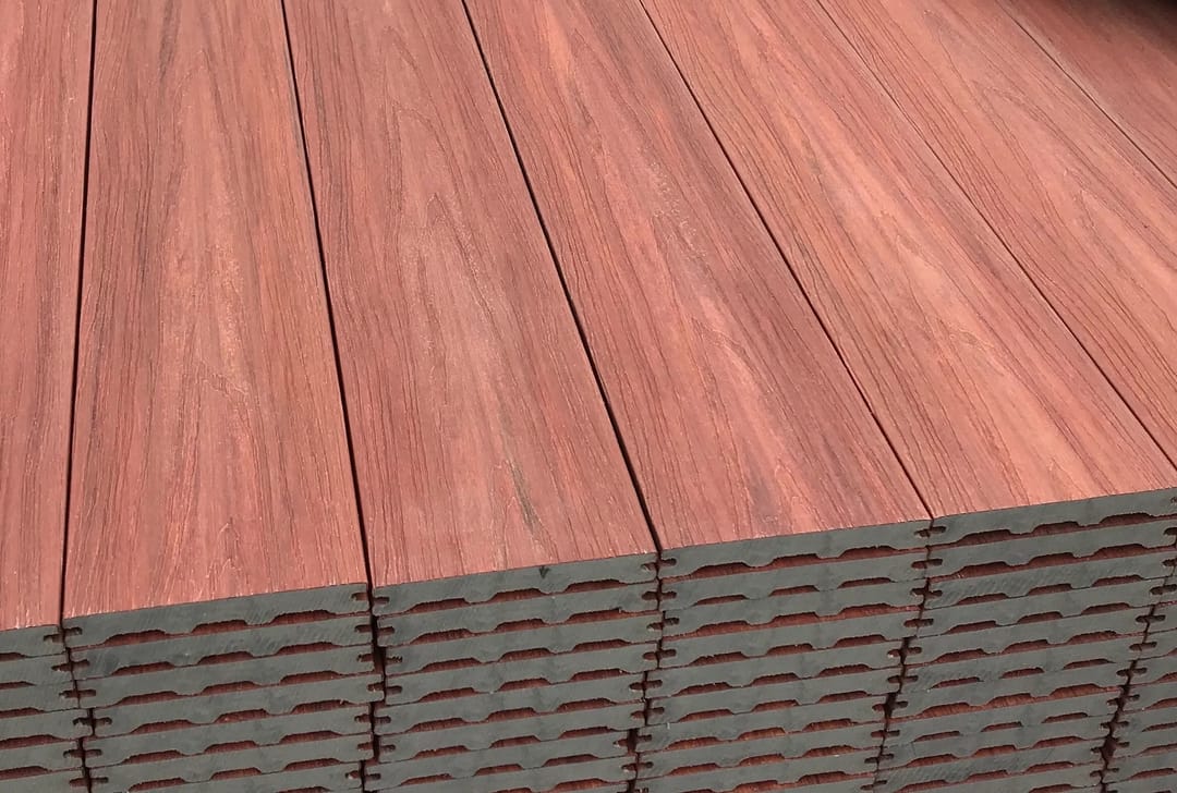 Stack of red-brown FreshDeck solid composite boards showing the wood-grain top face and board ends