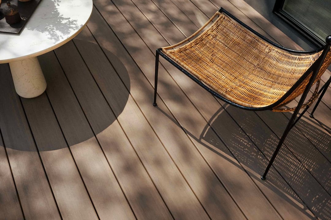 Dappled sunlight on English Walnut decking with a woven sling chair and round white side table