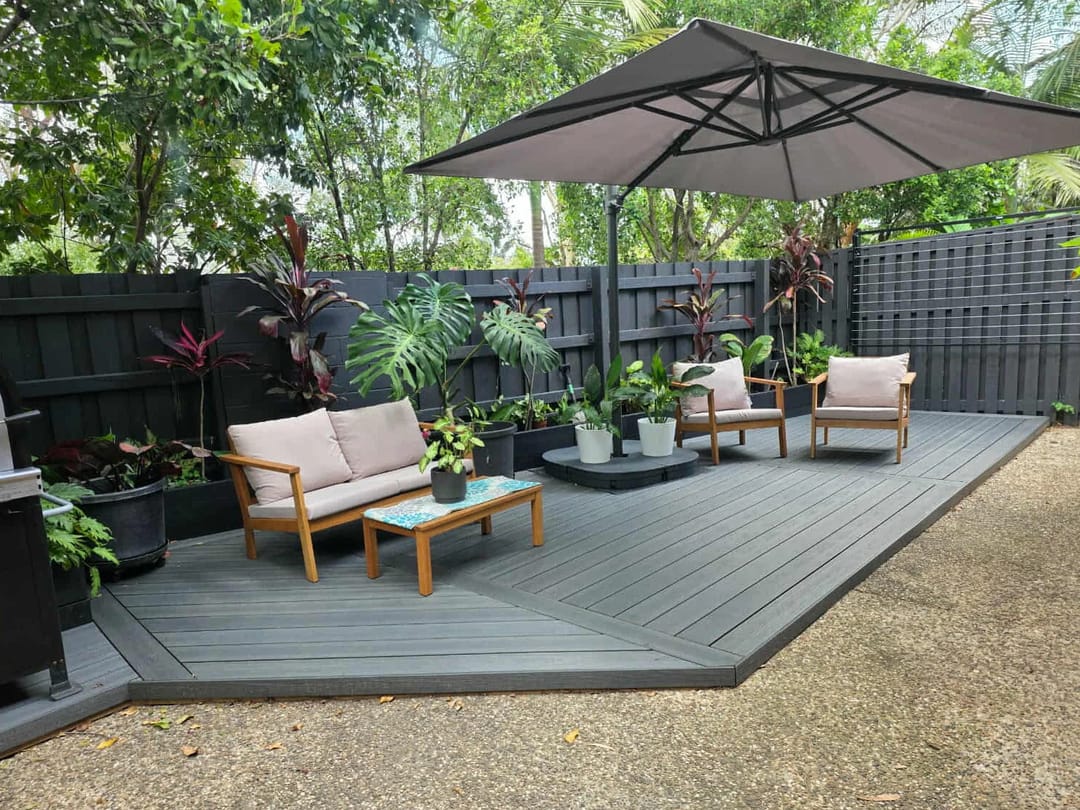 Dark grey composite courtyard deck with an outdoor sofa set, cantilever umbrella and tropical planting