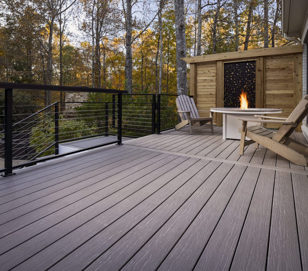 Cathedral Stone deck with cable railing, Adirondack chairs and a fire table by a timber fireplace wall in the woods