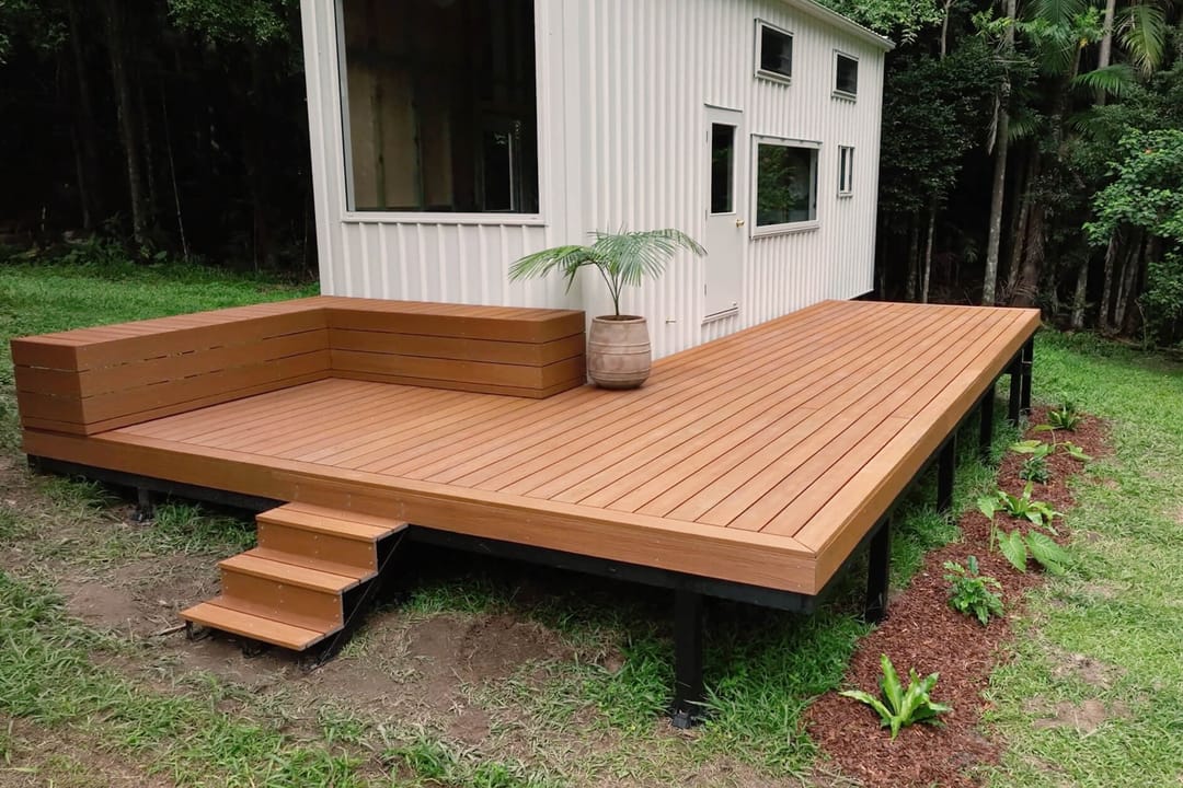 Raised Brite NextGen Titanium Tawny deck with built-in bench and steps beside a white tiny house in the Byron Bay hinterland
