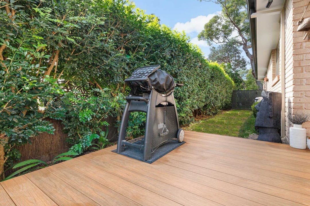 Backyard deck in Brite HD Urban X Teak Wood in Newport NSW with a barbecue on a stand and a tall green hedge