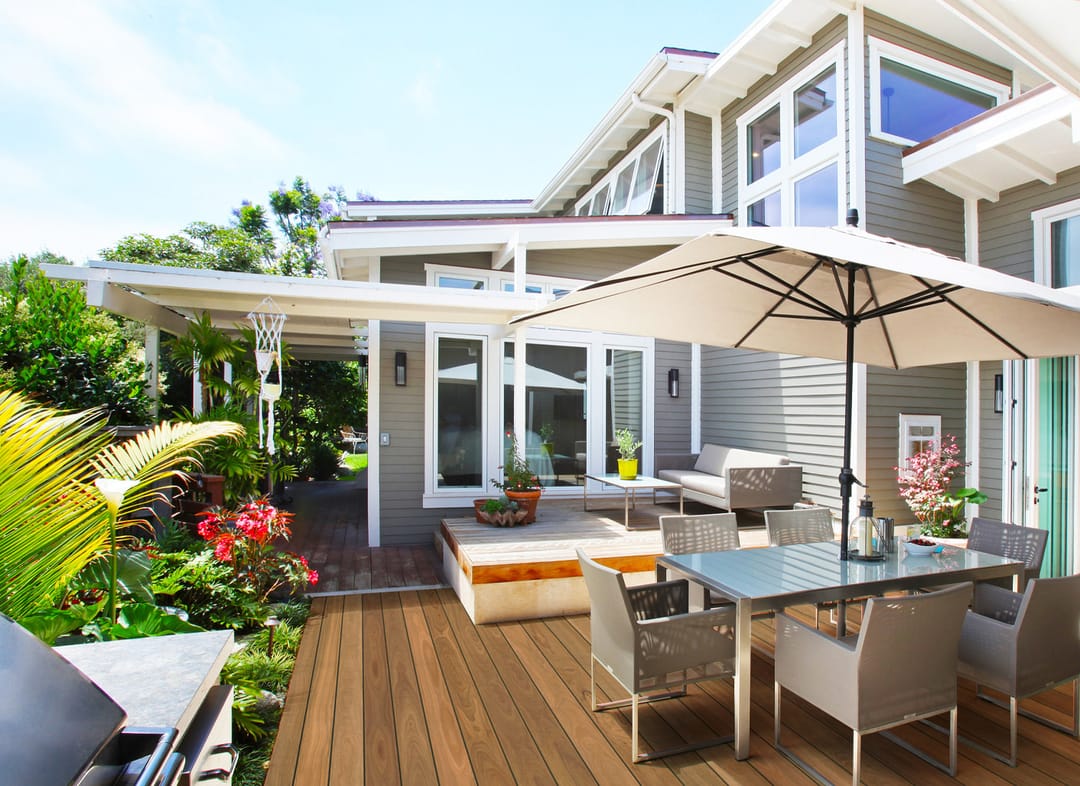Eva-Last Pioneer Spotted Gum deck in front of a grey weatherboard home with an umbrella, dining setting and flowering garden