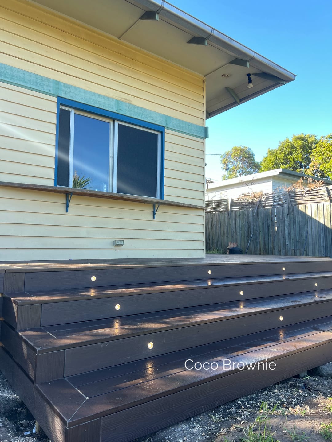 Dark brown Evertex Essence Coco Brownie deck with wide steps and step lights against a yellow weatherboard house