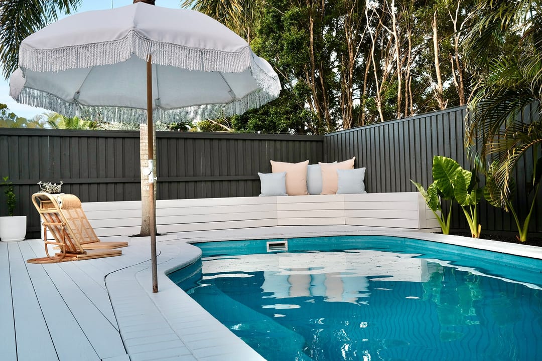 White Sun Decking Elite deck around a backyard pool, with a fringed umbrella, a lounge chair and dark fencing