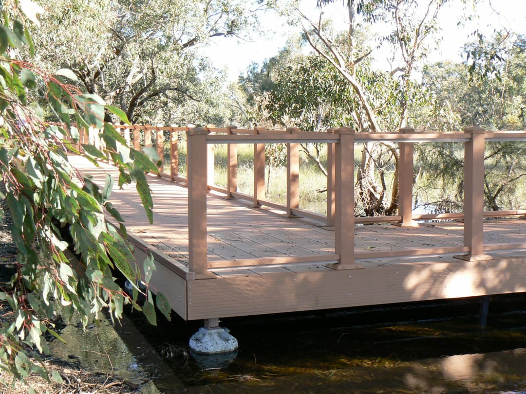 Composite deck platform with a timber-look balustrade set among trees beside water at Lightning Park