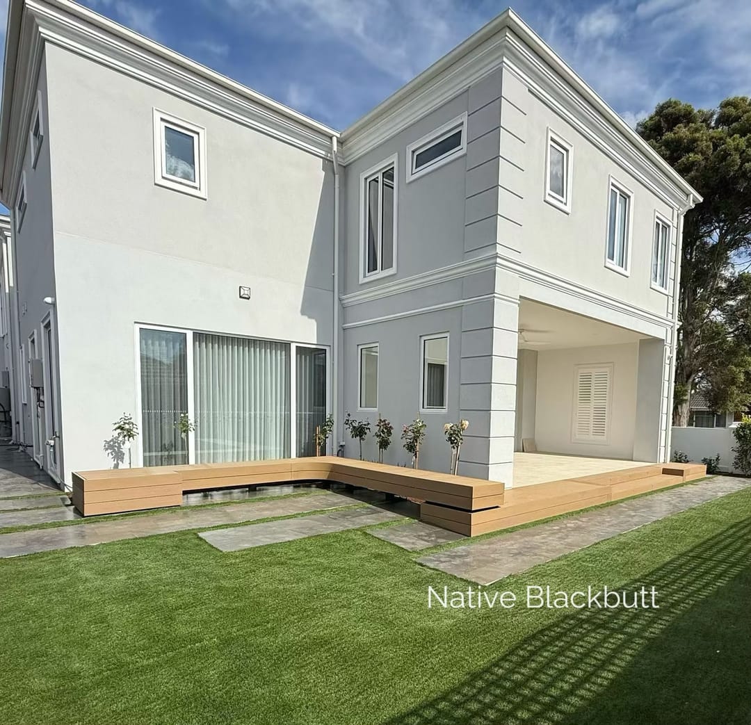 Low Evertex Essence Native Blackbutt deck along a white rendered two-storey house with synthetic lawn and stepping pavers