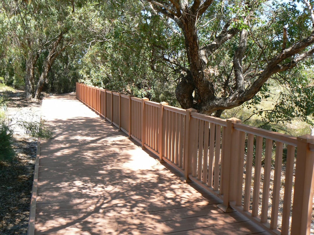 Narrow composite boardwalk with a timber-look balustrade through shaded bushland