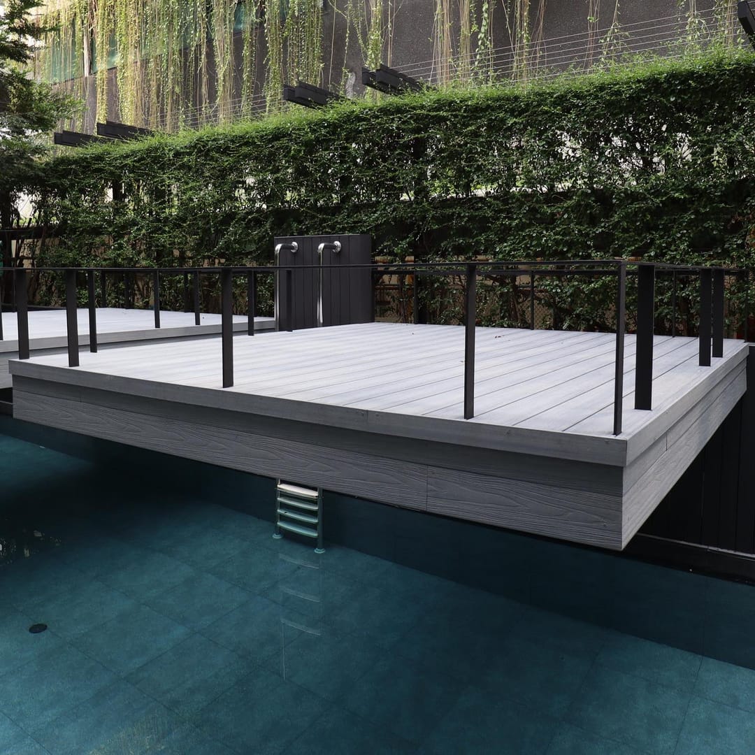 Pale grey PureSolid composite deck platform with black railing over a dark pool, a tall hedge behind