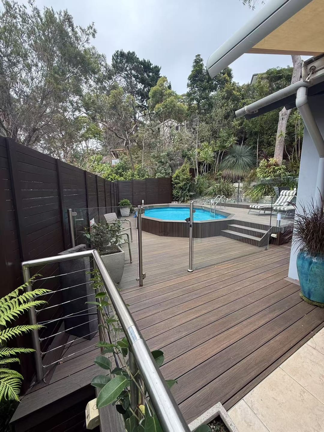 Mid-brown Acetech deck stepping down to a round spa, with a stainless wire balustrade, timber screen fence and garden