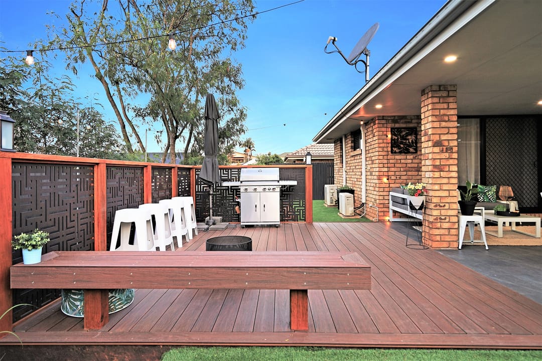 Backyard Sun Decking Elite Walnut deck with a built-in bench, red slat screen, barbecue and string lights