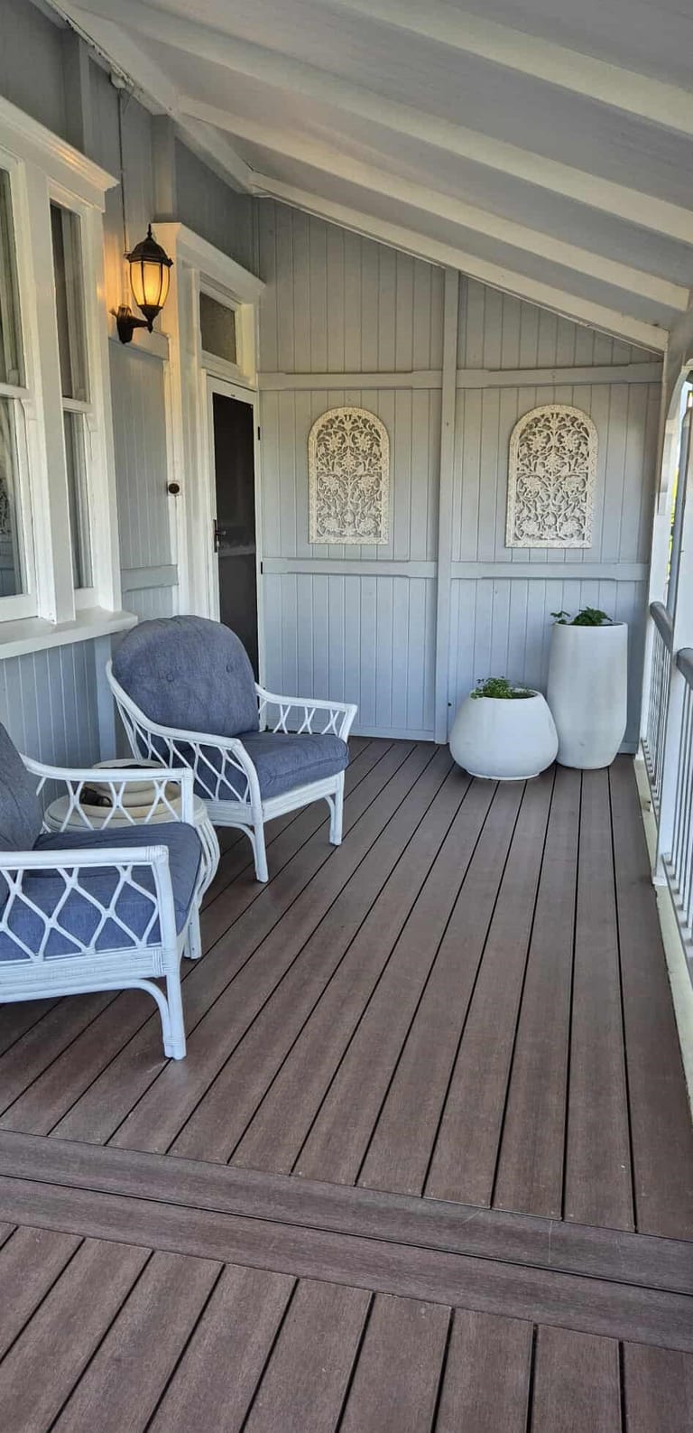 Brown composite deck on a Queenslander verandah with white wicker armchairs and decorative fretwork panels