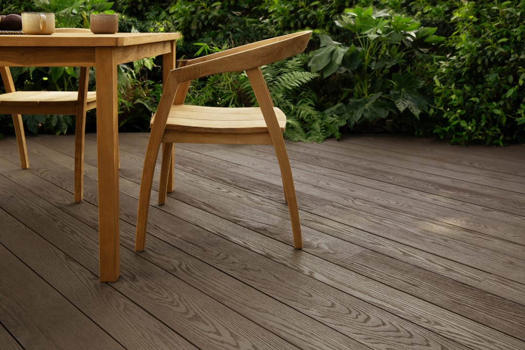 Dark Ebony Grey deck with a timber outdoor table and chairs against lush tropical planting