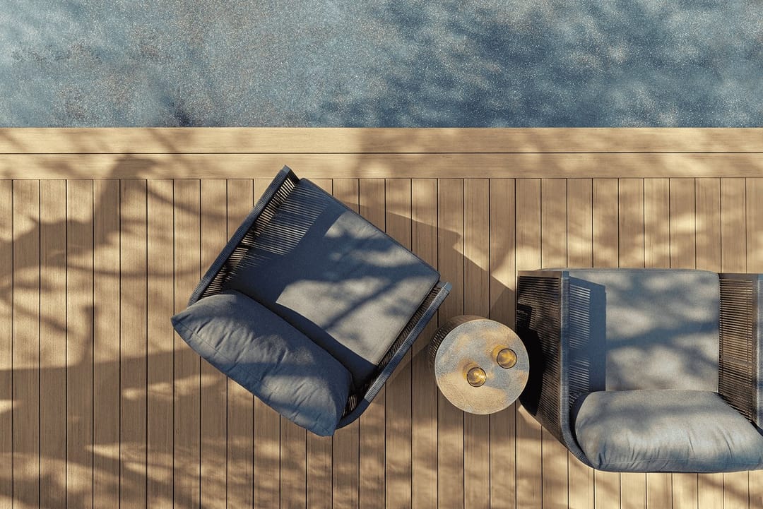 Overhead view of two blue-grey lounge chairs and a small side table on light brown Vintage decking near water