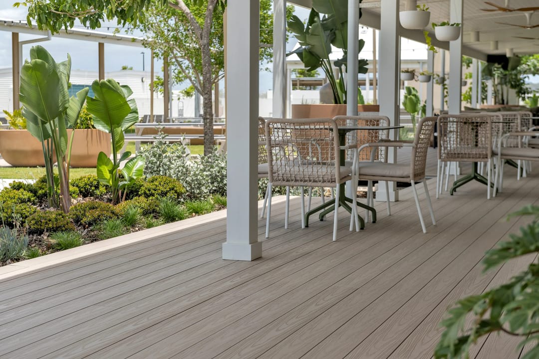 Pale grey-beige COEN composite verandah deck with outdoor dining tables and lush garden beds at a lifestyle community