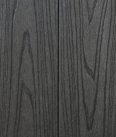 Two Modern Deck Classic Solid boards in Storm Grey, a dark grey-brown woodgrain-embossed composite surface shown close up