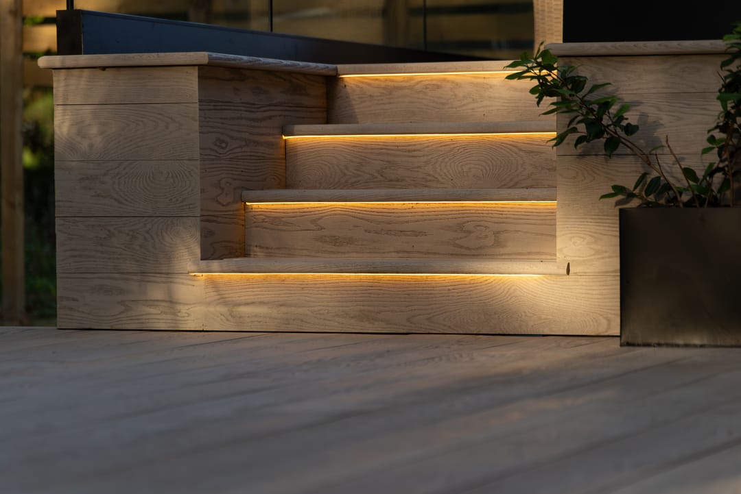 Pale Limed Oak deck at dusk with clad steps lit by LED strips leading up to a raised terrace