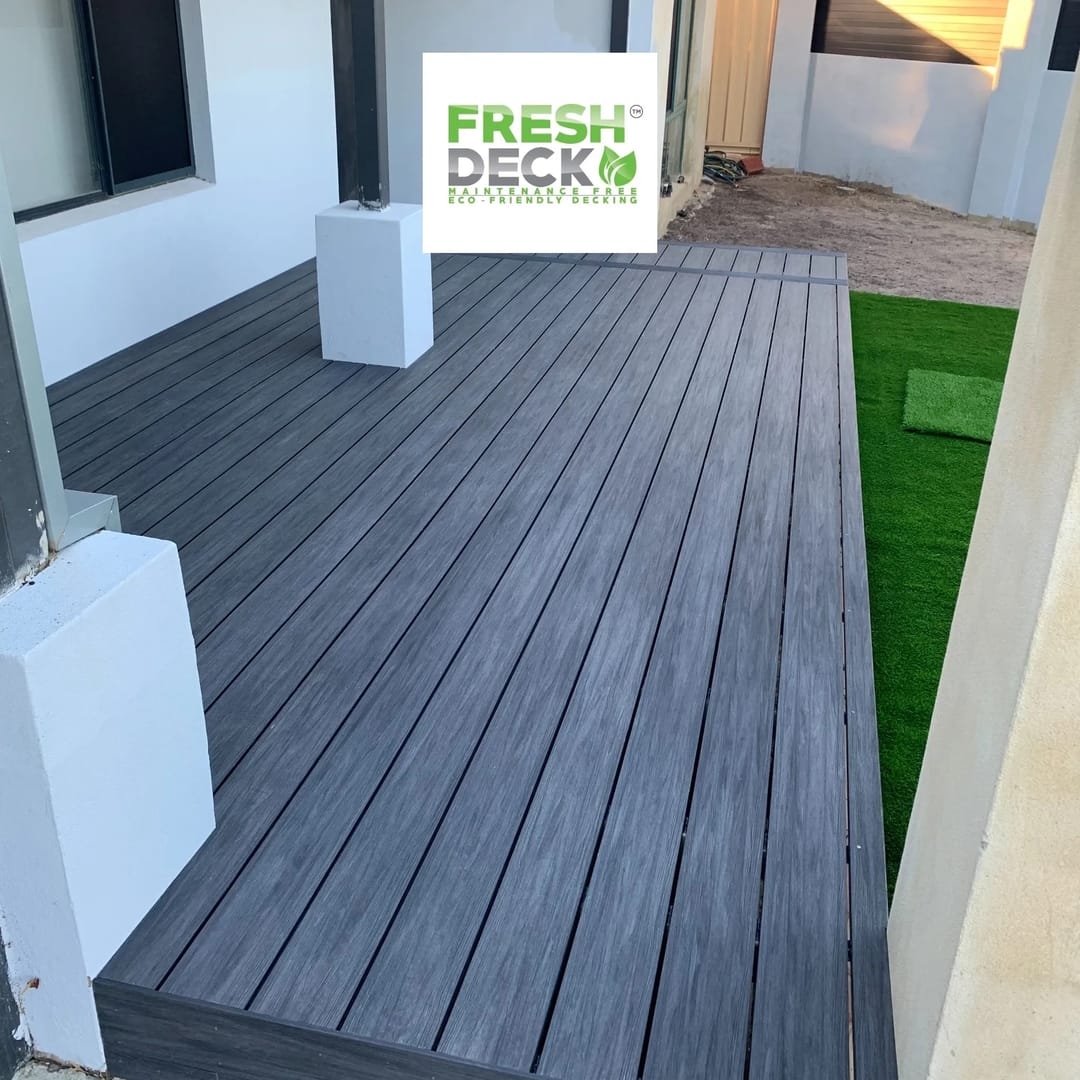 Grey FreshDeck composite deck filling a side courtyard next to a rendered wall and a strip of synthetic turf