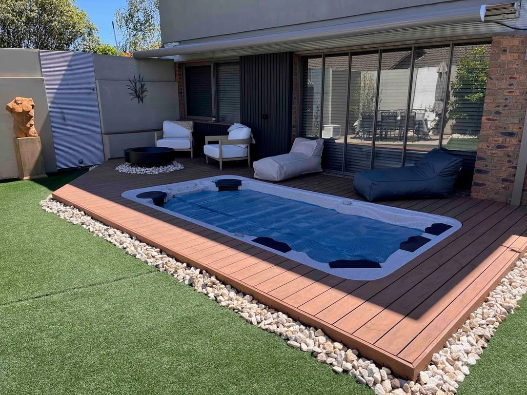 Black Bean CleverDeck boards framing an in-ground swim spa on artificial lawn, with outdoor lounges and a pebble border