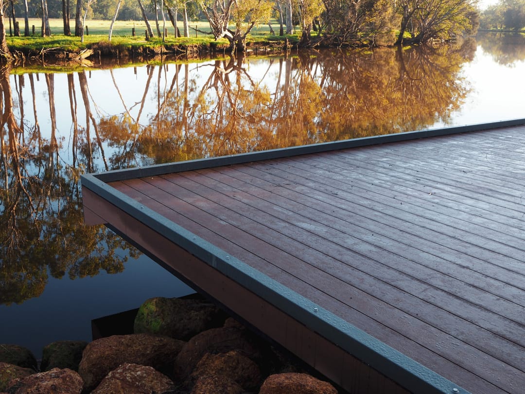 Brown composite platform with a dark fascia jutting over a river, autumn trees reflected in the water