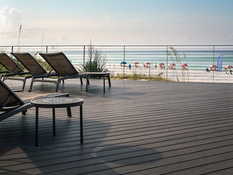 Beachfront Vision deck with sun loungers and a round table behind a glass and cable railing, the beach beyond