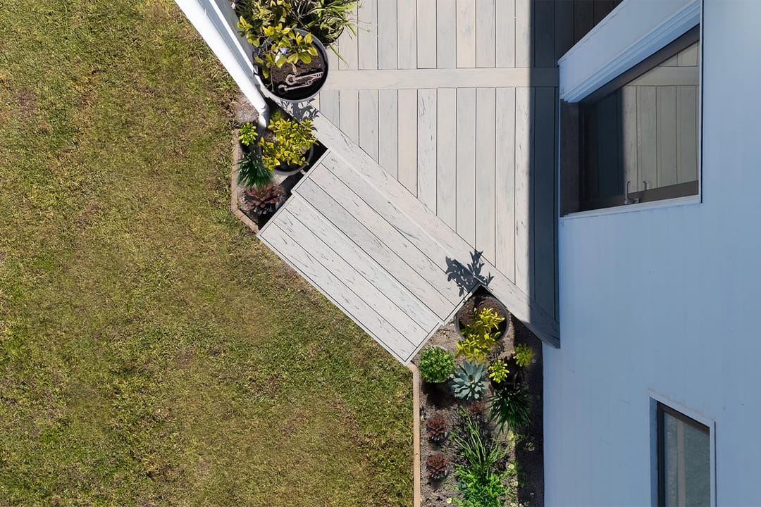 Overhead view of an angled OneDeck PVC deck and steps beside a rendered house, a lawn and succulent garden