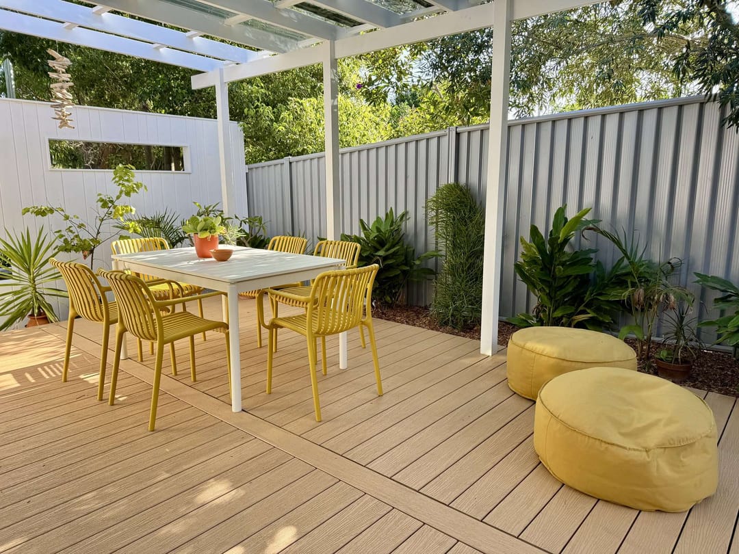 Pale ModWood Xtreme Guard Sandy Bay deck under a pergola with yellow outdoor dining chairs and ottomans