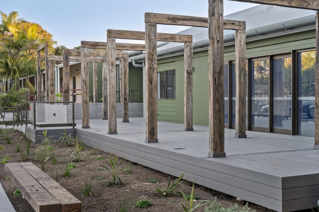Grey COEN composite deck with recycled timber posts and pergola beams along a community building in Byron Bay