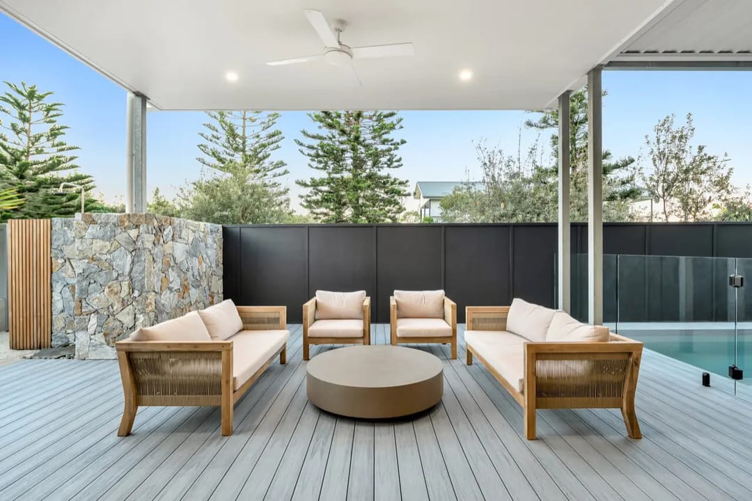 Colour visualisation of a covered alfresco deck in COEN Driftwood, a pale silver-grey, with outdoor lounges and a stone feature wall