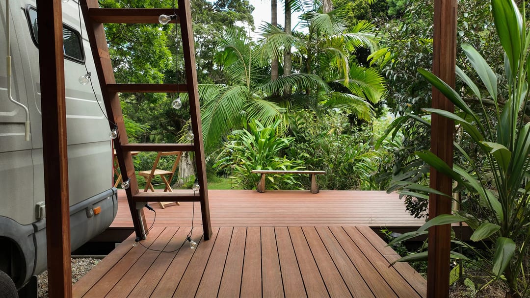 Ekodeck Designer Series Riverbank Red deck in a lush tropical garden beside a timber ladder and camper